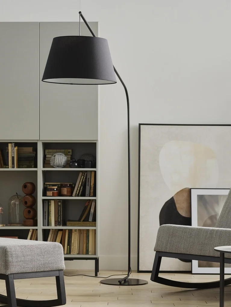 Czarna, minimalistyczna lampa podłogowa w salonie, obok regału z książkami .